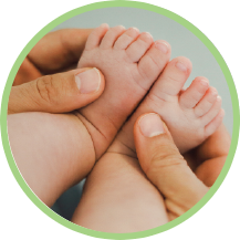 Tiny baby feet standing in the cupped hands of a human. Baby toes are wrapped around the forefingers of each hand. One thumb, from each hand, rests on top of each baby foot.